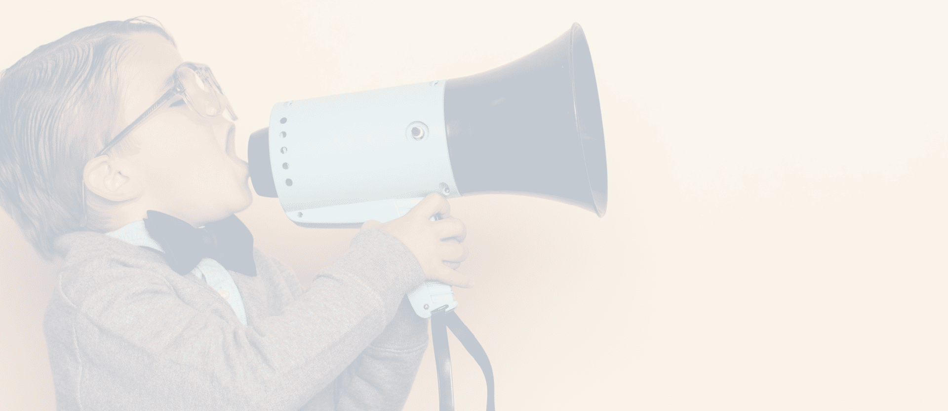 A young nerd boy yells into a megaphone in the studio. He is wearing a bow tie and eyeglasses. He wants you to listen to his important message.