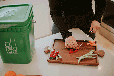 woman chops vegetables next to compost container