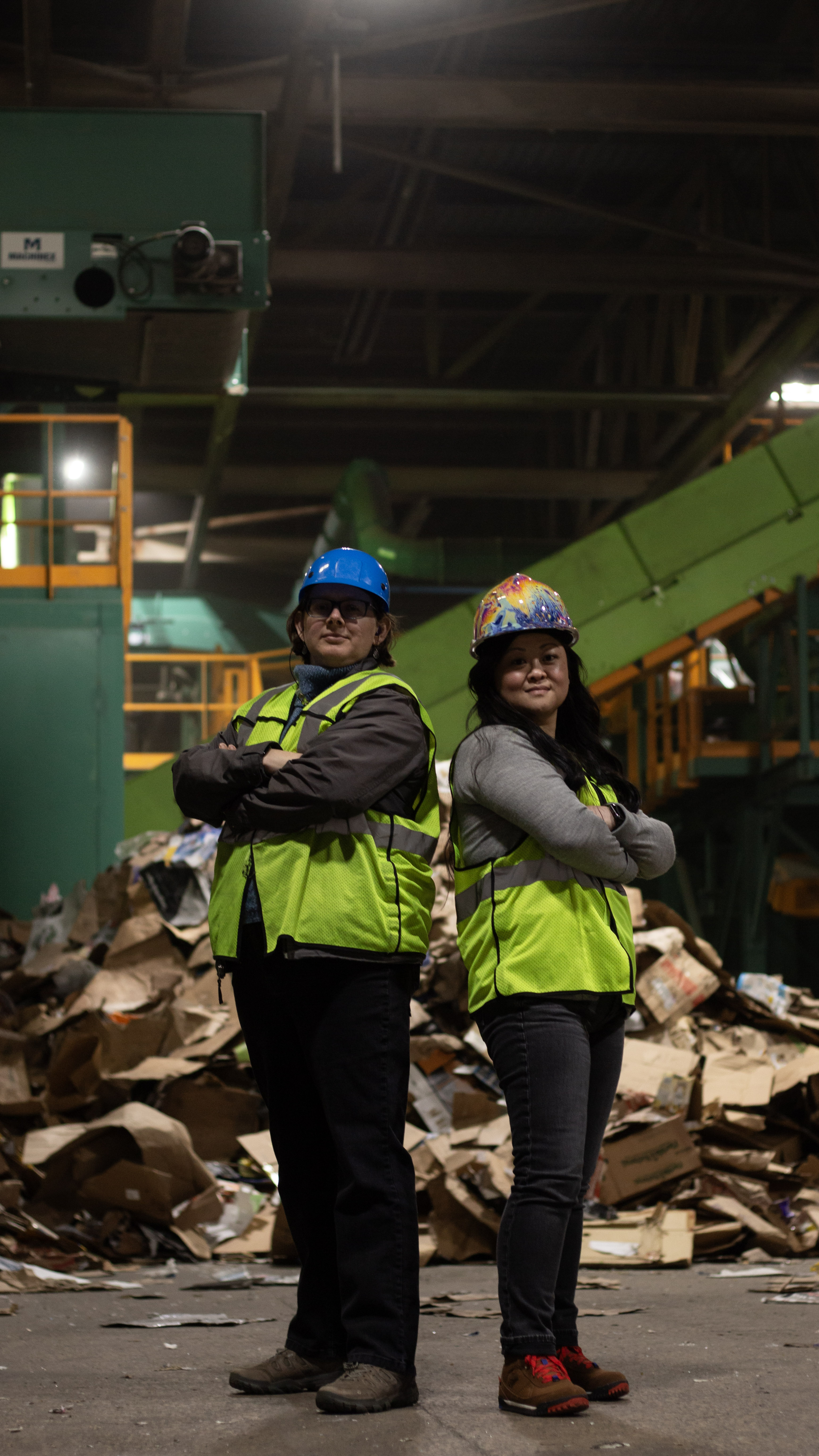 two women posing back to back in a recycling facility