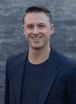 a smiling man in a back t-shirt and grey suit jacket