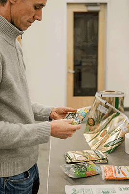 a white man in a grey sweater examines flexible plastic packaging