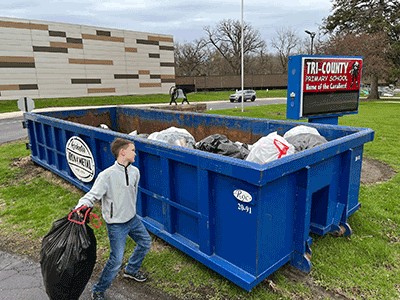 boy throwing bag of cans into a roll-off
