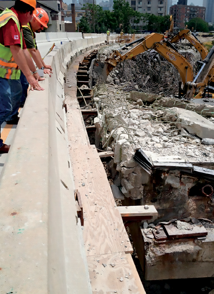 two people in work vests and hard hats look down into construction zone