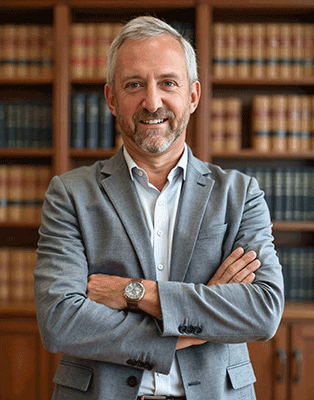 a caucasian man with grey hair and a beard in a suit jacket with his arms crossed over his chests