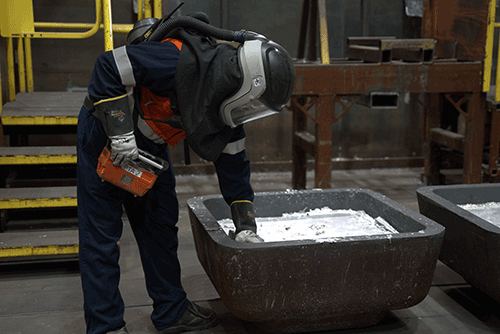a person in safety gear bends over molten aluminum